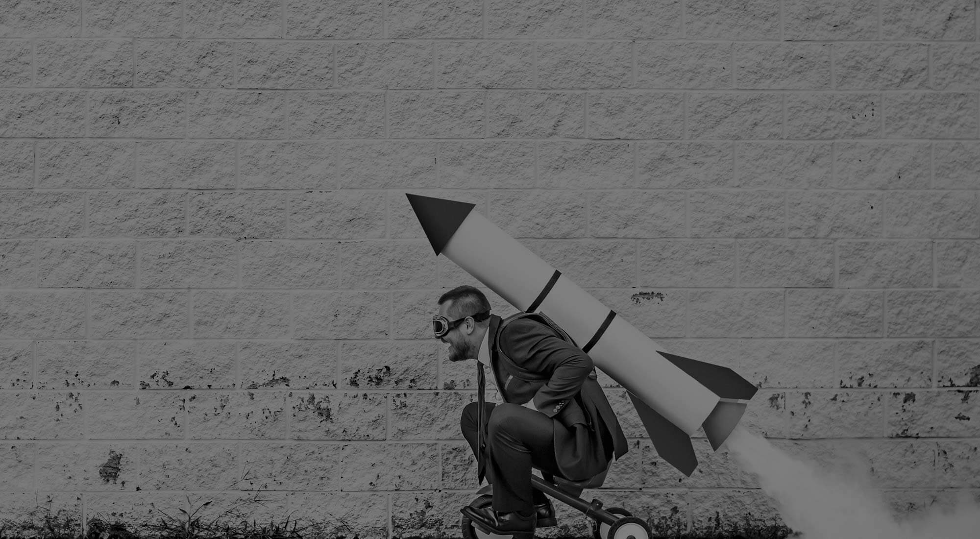 man sitting on small tricycle with a fake rocket attached to his back